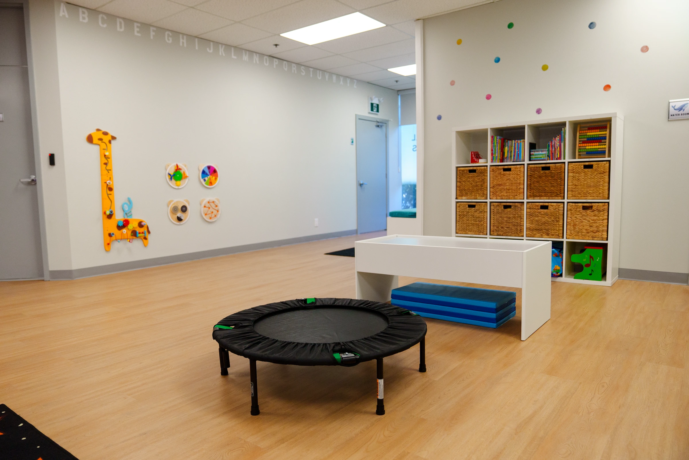 A large playroom with wooden floors, white walls, and a small trampoline.